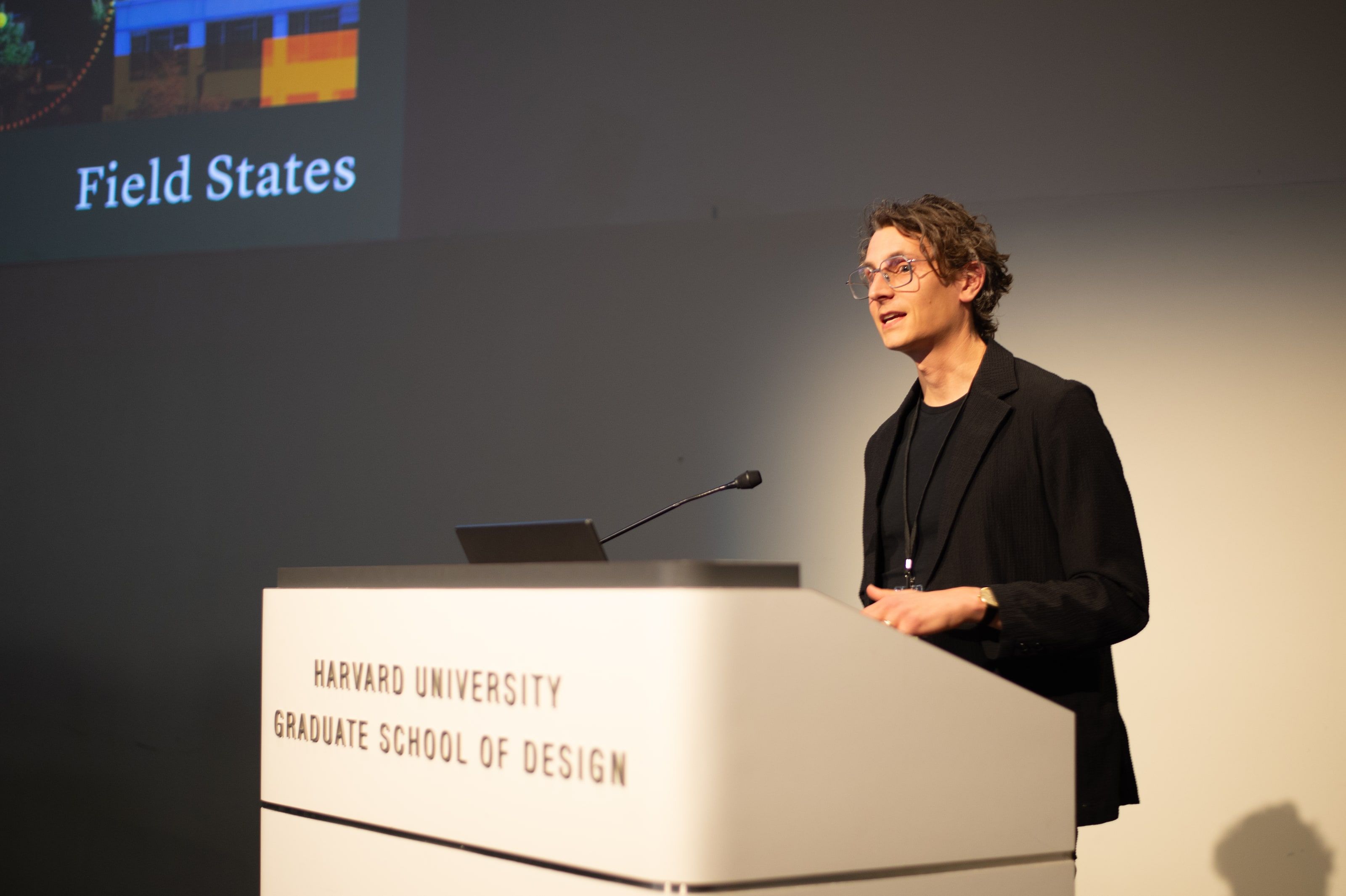 Matthew Claudel speaking at a lectern marked Harvard University Graduate School of Design, beneath a projected slide that reads Field States.